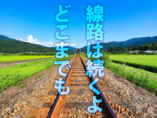 A railroad track stretching across a rural field into the blue sky.